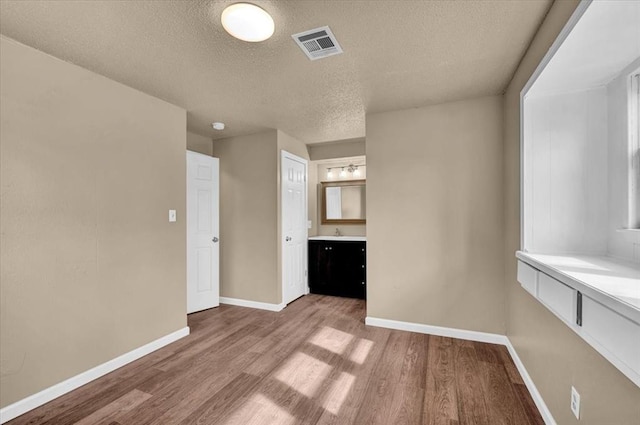 empty room featuring a textured ceiling, wood finished floors, visible vents, and baseboards