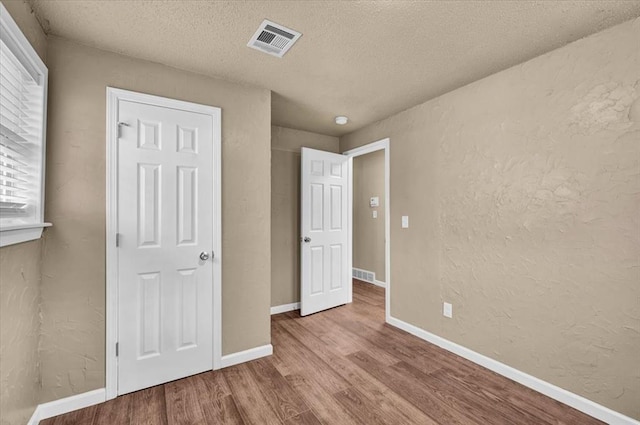 unfurnished bedroom with a textured wall, wood finished floors, visible vents, and baseboards