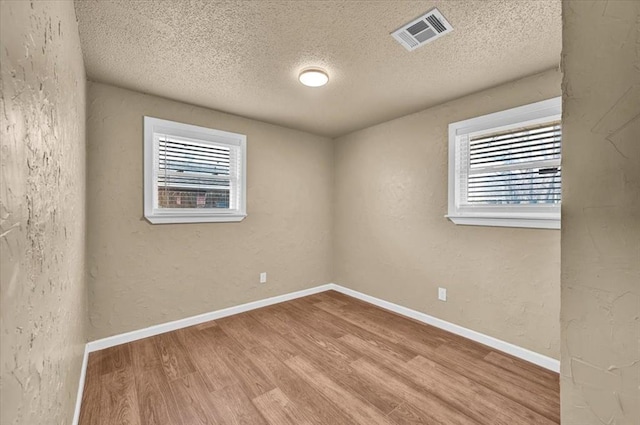 empty room with baseboards, visible vents, wood finished floors, and a textured wall