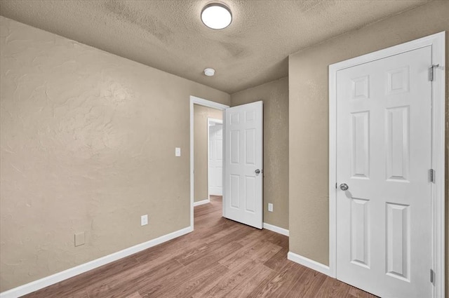 unfurnished bedroom with a textured ceiling, a textured wall, wood finished floors, and baseboards