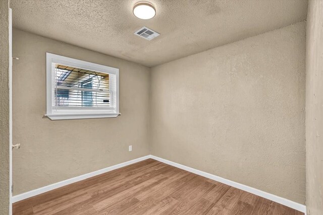 unfurnished room featuring baseboards, visible vents, wood finished floors, and a textured wall