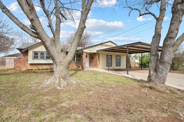 view of front of home featuring brick siding, fence, concrete driveway, a carport, and a front lawn