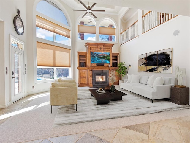 living area with ceiling fan, a high ceiling, baseboards, a glass covered fireplace, and crown molding