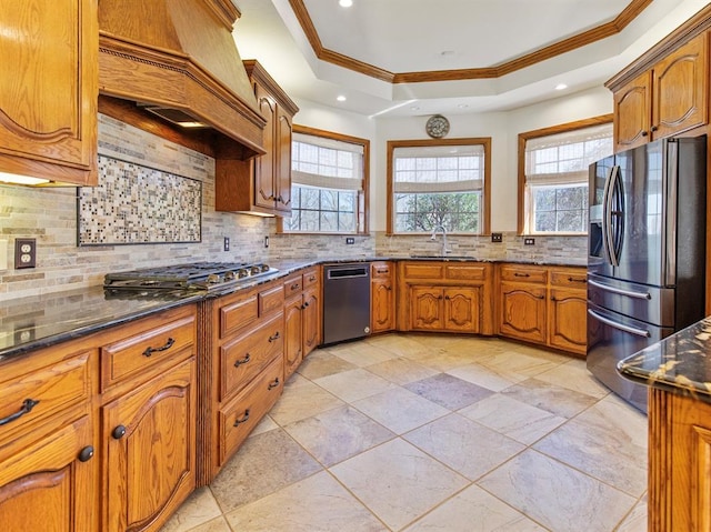 kitchen featuring premium range hood, a sink, appliances with stainless steel finishes, brown cabinetry, and a raised ceiling