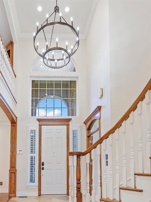 entrance foyer with baseboards, a towering ceiling, ornamental molding, stairs, and a chandelier