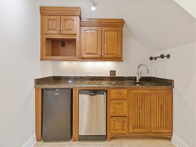 kitchen with lofted ceiling, a sink, dark stone countertops, dishwasher, and fridge