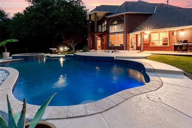 pool at dusk featuring a patio area, a grill, and a pool with connected hot tub