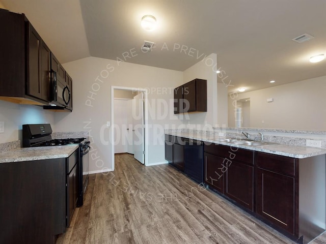 kitchen with a peninsula, wood finished floors, a sink, dark brown cabinets, and black appliances