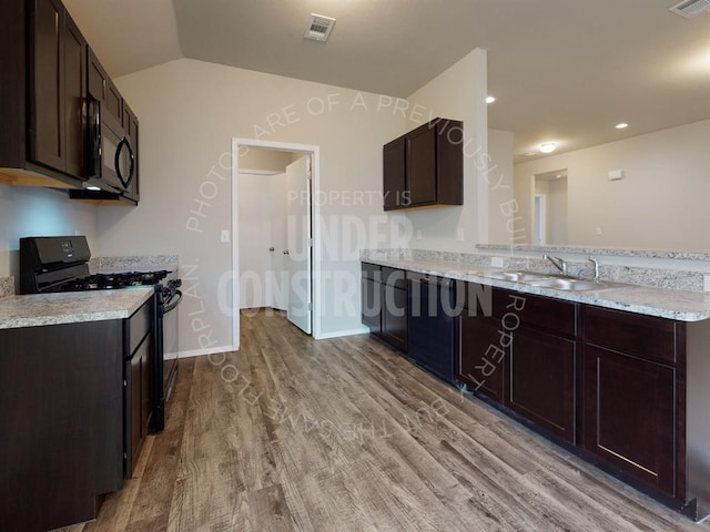 kitchen with a peninsula, wood finished floors, a sink, dark brown cabinets, and black appliances