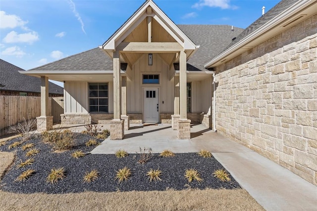 entrance to property with board and batten siding, stone siding, roof with shingles, and fence