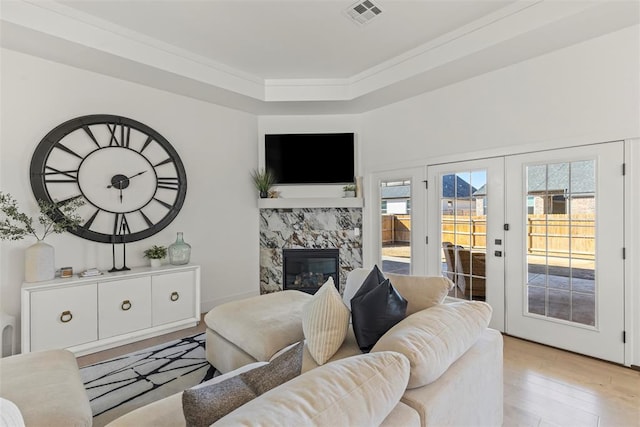 living area with french doors, a fireplace, visible vents, ornamental molding, and light wood-type flooring