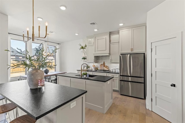 kitchen with a notable chandelier, stainless steel appliances, visible vents, dark countertops, and a center island with sink