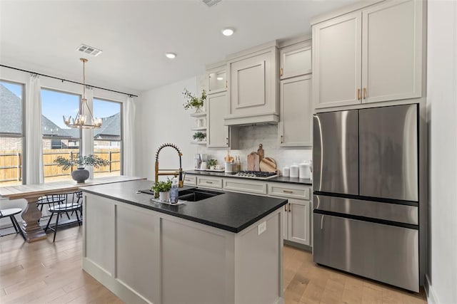 kitchen with stainless steel appliances, a sink, visible vents, tasteful backsplash, and dark countertops