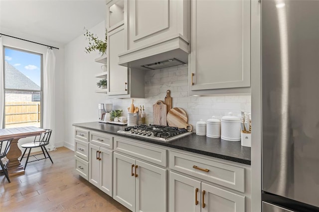 kitchen with open shelves, stainless steel appliances, dark countertops, decorative backsplash, and premium range hood