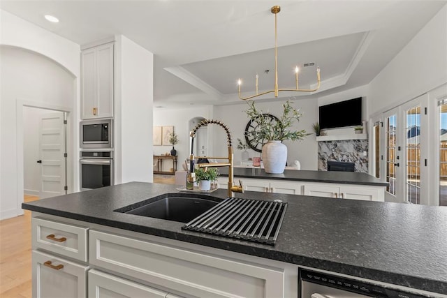 kitchen featuring a raised ceiling, appliances with stainless steel finishes, light wood-style floors, white cabinetry, and a sink