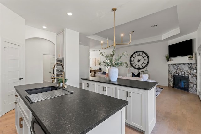 kitchen with a sink, light wood-style floors, open floor plan, a center island, and a tray ceiling