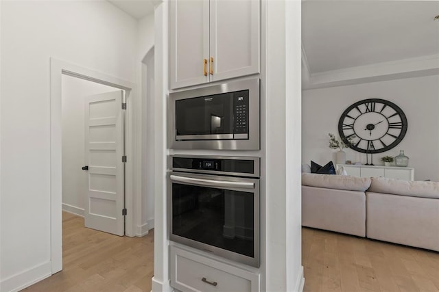 kitchen with ornamental molding, built in microwave, oven, and light wood-style flooring