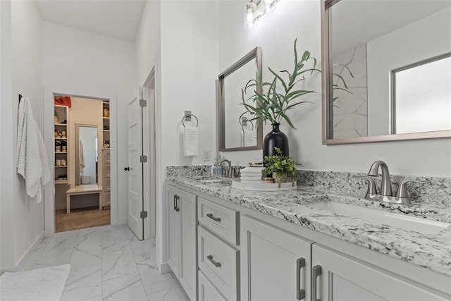 full bath featuring marble finish floor, double vanity, a sink, and baseboards