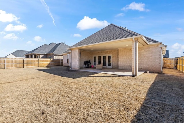 rear view of house featuring a patio, a fenced backyard, roof with shingles, french doors, and brick siding