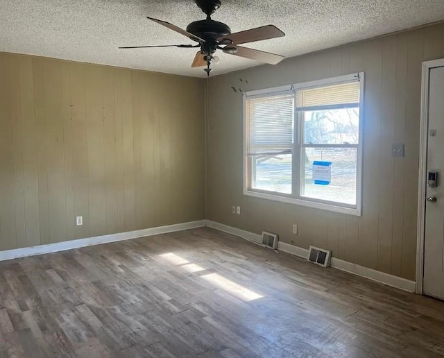 empty room featuring a textured ceiling, wood finished floors, a ceiling fan, visible vents, and baseboards