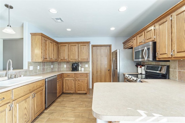 kitchen featuring a peninsula, a sink, light countertops, appliances with stainless steel finishes, and tasteful backsplash