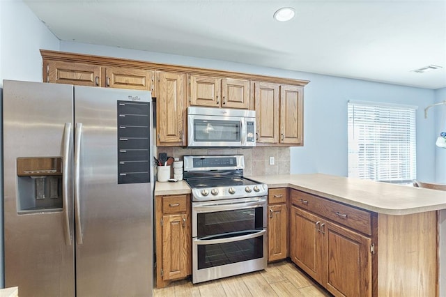 kitchen with a peninsula, light countertops, light wood-style floors, appliances with stainless steel finishes, and tasteful backsplash