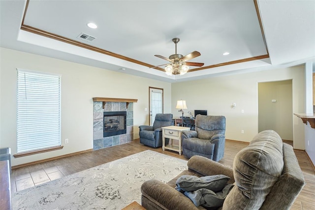 living area featuring visible vents, a tile fireplace, a raised ceiling, and wood finished floors