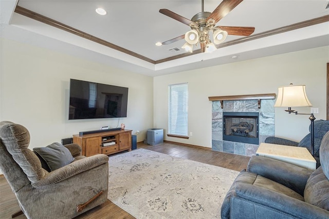 living room with visible vents, crown molding, a tile fireplace, wood finished floors, and a raised ceiling