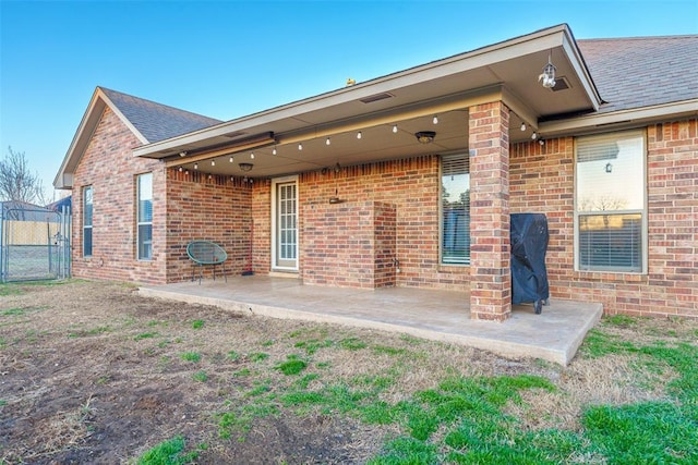 back of property with brick siding, fence, a patio, and roof with shingles