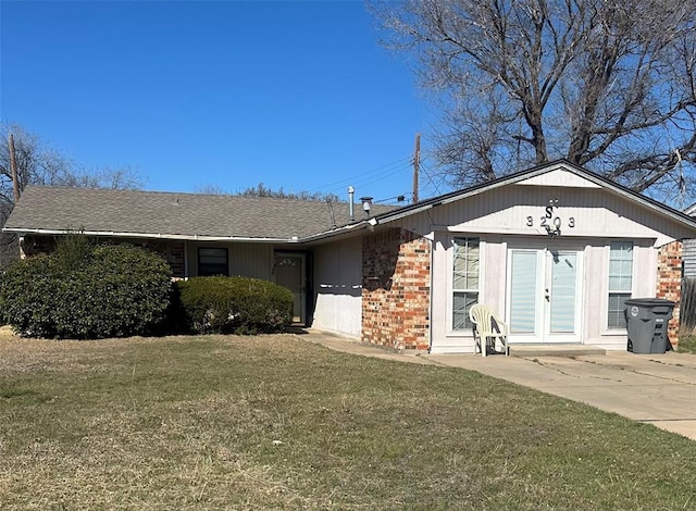 view of front of home with a shingled roof, a front yard, and brick siding