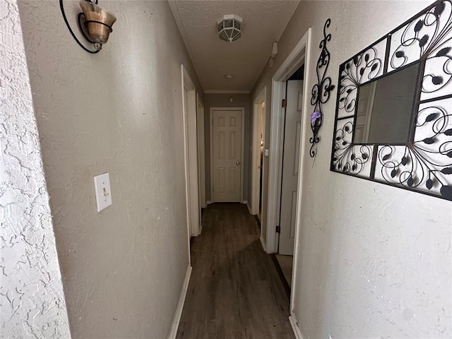 hall with a textured ceiling, a textured wall, wood finished floors, and baseboards