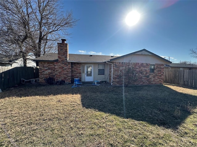 back of property with a chimney, fence, a lawn, and brick siding