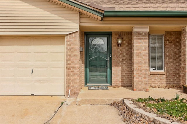 entrance to property featuring a garage, a shingled roof, and brick siding