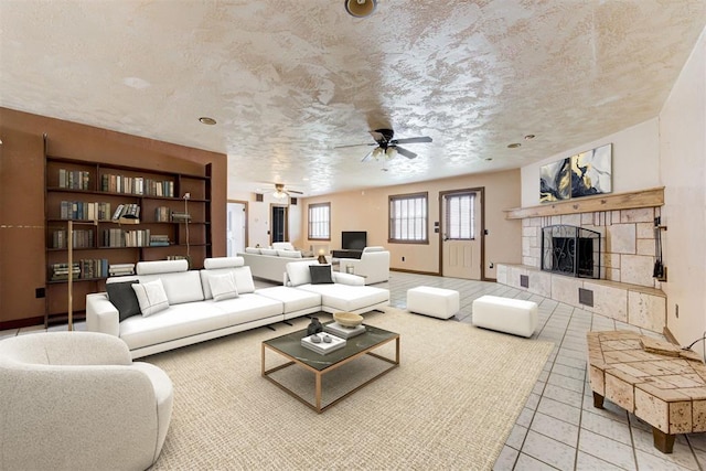 tiled living room featuring ceiling fan, a fireplace, baseboards, and a textured ceiling