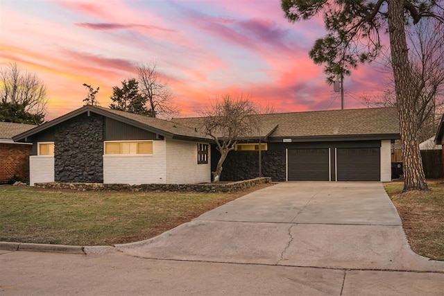 view of front of home featuring a shingled roof, concrete driveway, stone siding, an attached garage, and a front yard