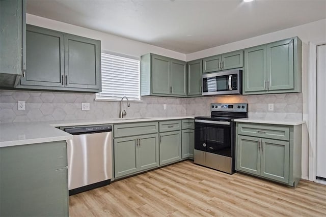 kitchen with appliances with stainless steel finishes, green cabinetry, a sink, and light wood finished floors