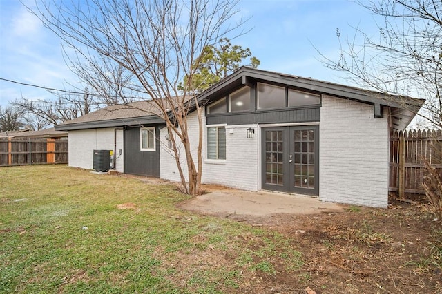 rear view of house with central AC, brick siding, fence, a yard, and french doors