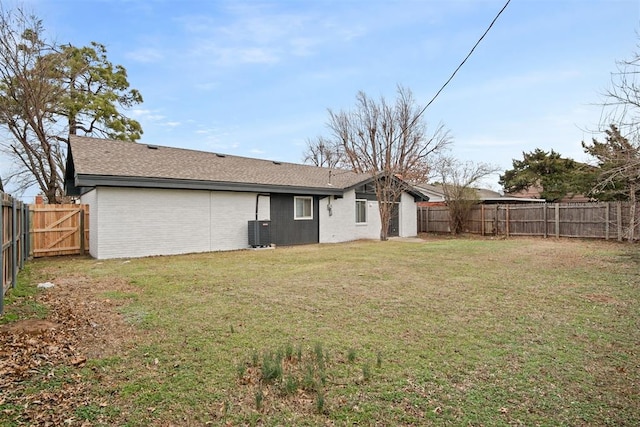 rear view of property featuring a shingled roof, central AC unit, a fenced backyard, a yard, and brick siding