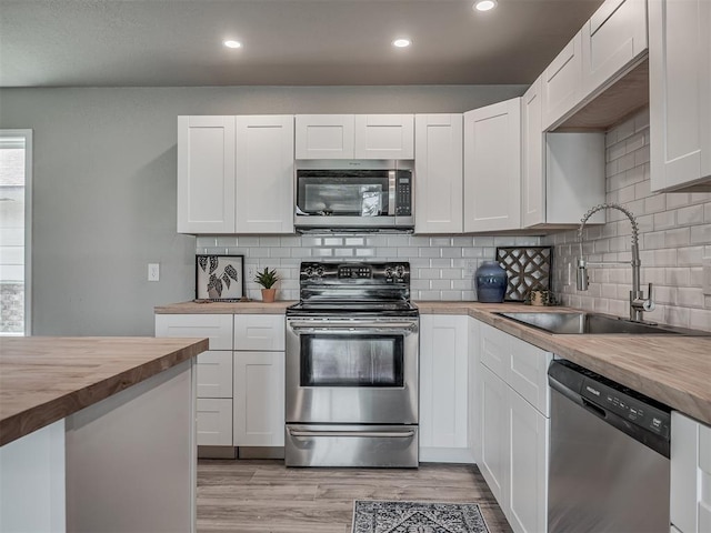 kitchen featuring light wood finished floors, recessed lighting, butcher block counters, appliances with stainless steel finishes, and a sink