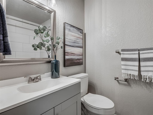 bathroom featuring a textured wall, vanity, and toilet