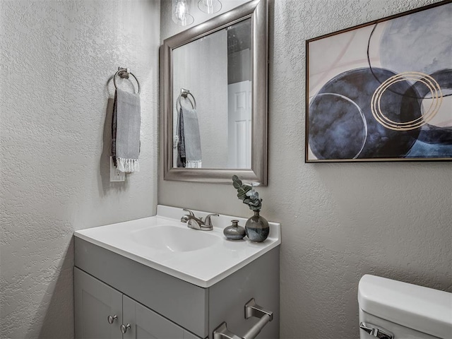 half bath featuring toilet, a textured wall, and vanity