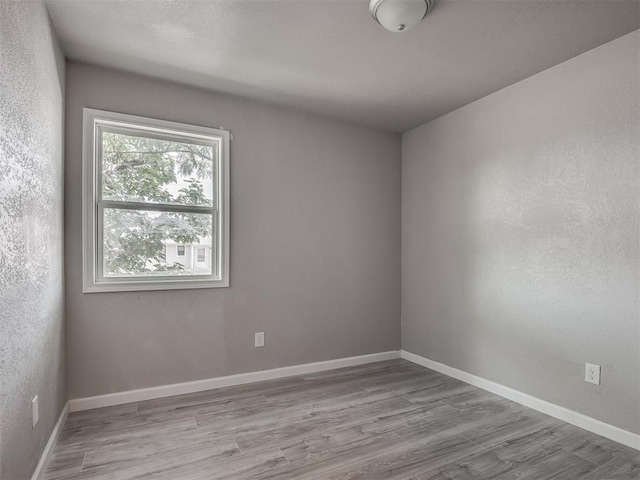 unfurnished room featuring a textured wall, wood finished floors, and baseboards