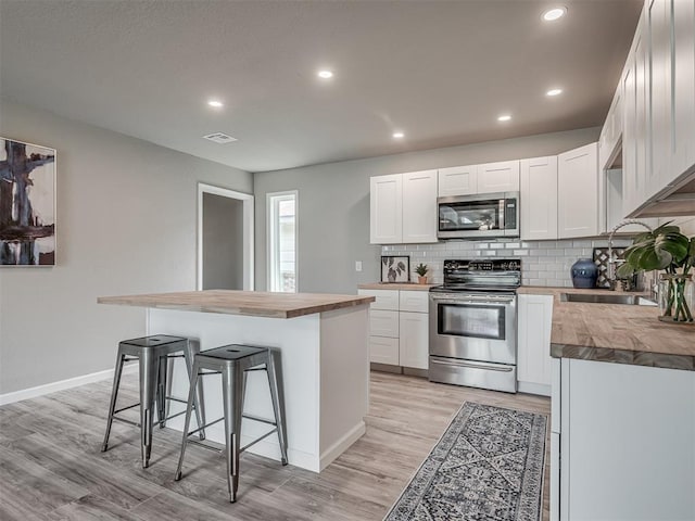 kitchen with decorative backsplash, a kitchen breakfast bar, stainless steel appliances, wooden counters, and a sink