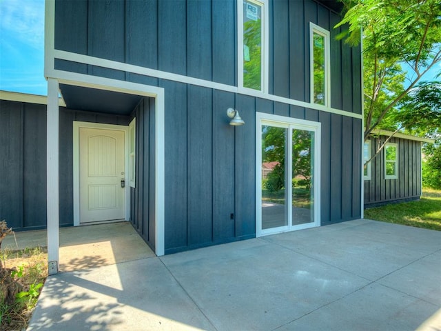 view of exterior entry with board and batten siding and a patio