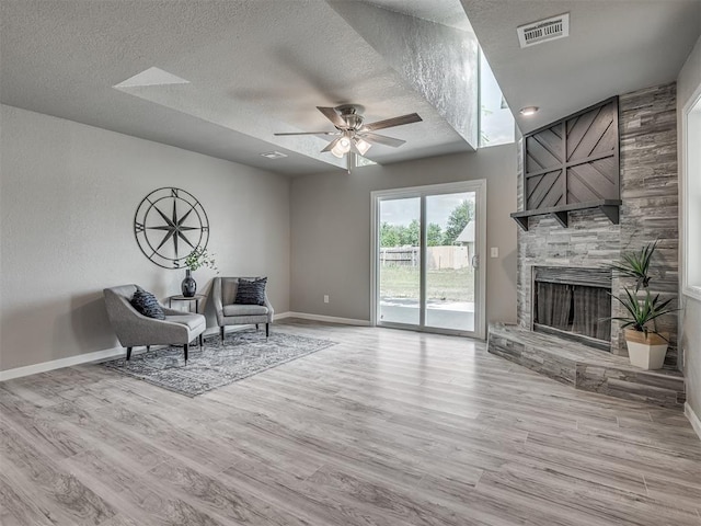 living area featuring visible vents, a stone fireplace, a textured ceiling, wood finished floors, and baseboards