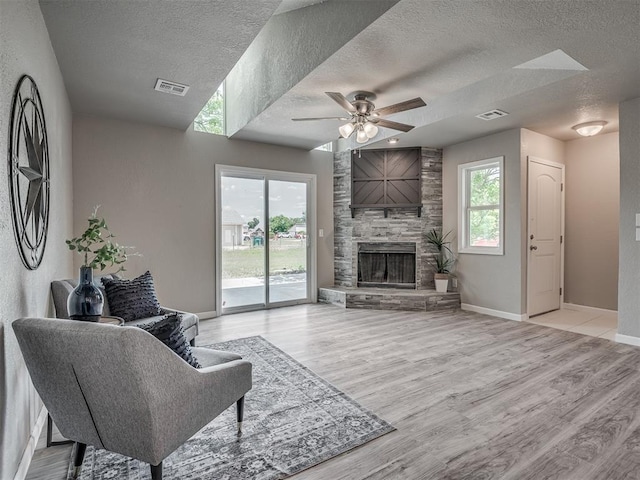 living area featuring light wood-type flooring, visible vents, ceiling fan, and a stone fireplace