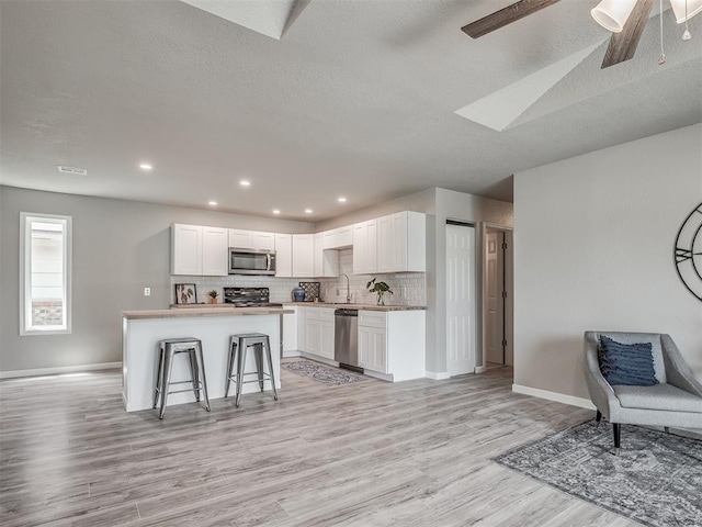 kitchen featuring tasteful backsplash, stainless steel appliances, light wood-type flooring, white cabinetry, and a sink