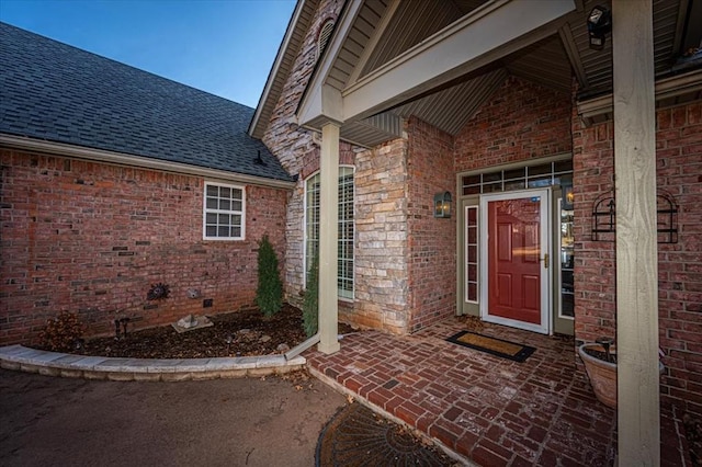 doorway to property with a shingled roof and brick siding