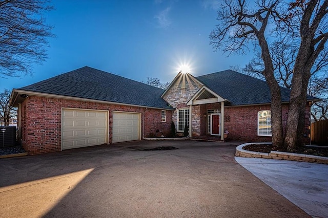 view of front of property featuring roof with shingles, driveway, brick siding, and central AC unit