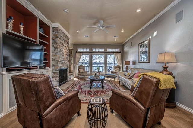 living room featuring ornamental molding, visible vents, a stone fireplace, and wood finished floors